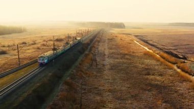 Bir banliyö treni şafakta yolcu taşır. Drone görünümü.