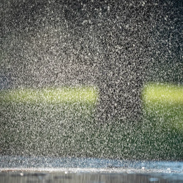 Caen gotas de lluvia sobre el asfalto y la hierba verde. — Foto de Stock