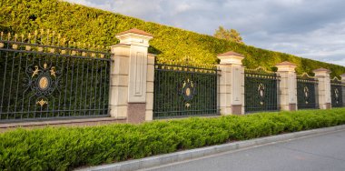 Yeşil thuja çalıları geometrik şekillere bürünür. Yol yapımı demir çit ve yüksek kaliteli asfalt. Seçkin bir köy kasabasında modern bir yol.