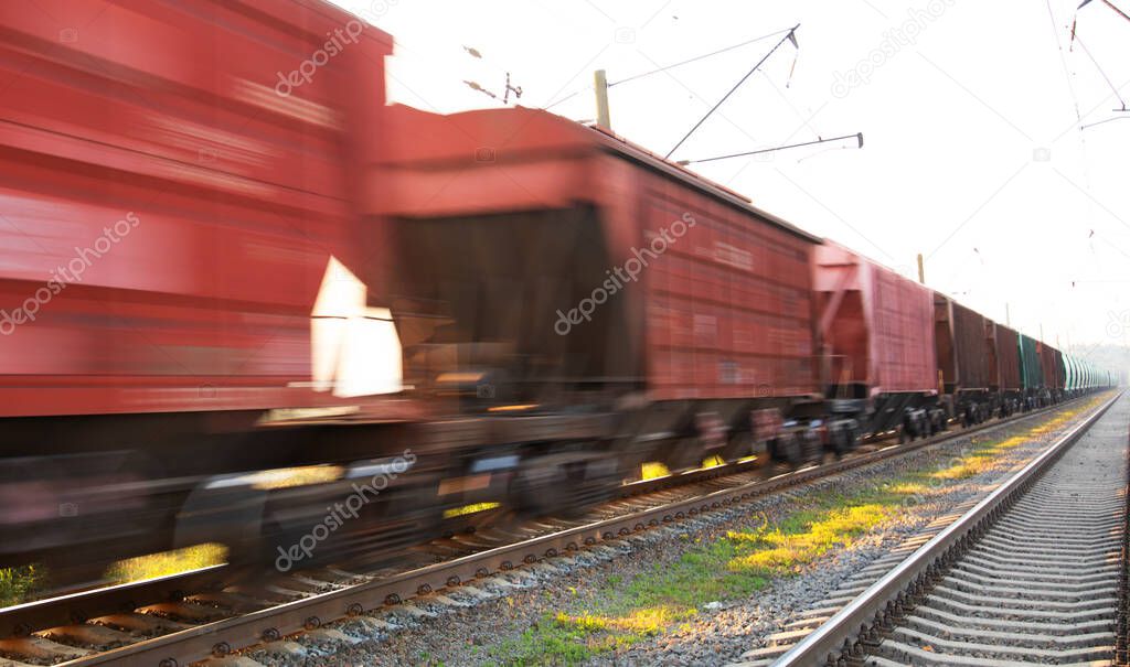 A freight train loaded with resources delivers cargo through the forest. Wonderful summer landscape. Blurred pine trees at dawn from spoiling rail.