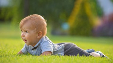 Cheerful smiling baby, little boy sitting on the lawn. Selective focus.
