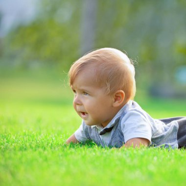 Neşeli gülümseyen bir bebek, çimenlerde oturan küçük bir çocuk. Seçici odak.