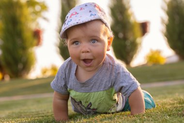 A cheerful kid is sitting on the lawn grass near the house. Recreation in the fresh air. A wonderful warm summer day.