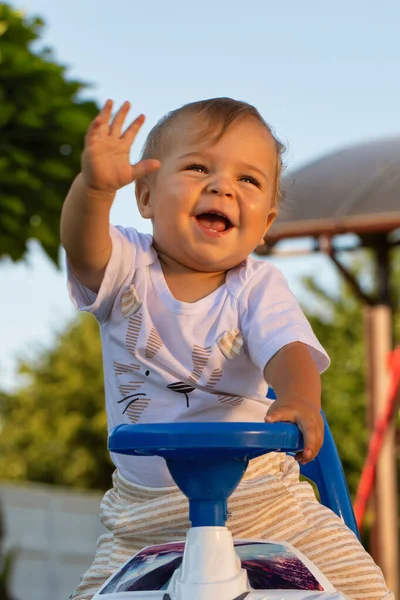 A little boy rides a toy police car in the park. Waving cheerfully. Large fire. Recreation in the fresh air. A walk in the park.