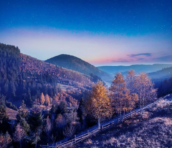 Night in the autumn mountains. Starry sky, yellow leafy trees and fog. A wonderful mountain landscape. Popular tourist destination.