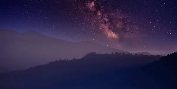 Night in the autumn mountains. Starry sky, yellow leafy trees and fog. A wonderful mountain landscape. Popular tourist destination.