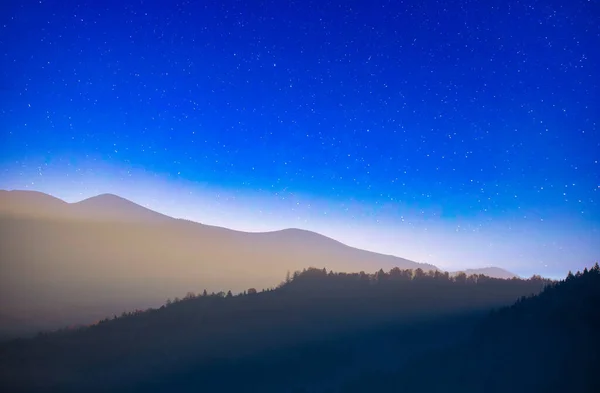 Night in the autumn mountains. Starry sky, yellow leafy trees and fog. A wonderful mountain landscape. Popular tourist destination.