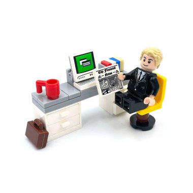 A Businessman working on office table with desktop computer. Lego figure photography concept idea.