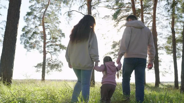 Felices caminatas familiares en el bosque, tomados de la mano en primavera, verano. Papá, niño, hija, mamá están jugando en el parque, el niño feliz está sosteniendo a los padres de la mano y saltando. Trabajo en equipo. Fin de semana familiar, infancia — Foto de Stock