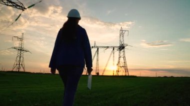 İnşaat mühendisi, kadın elektrik tedarikçisi açık havada çalışıyor. Çevre dostu elektrik. Modern teknolojiler. Güvenlik kaskındaki güç mühendisi güç hattını ve dijital tableti kontrol ediyor.