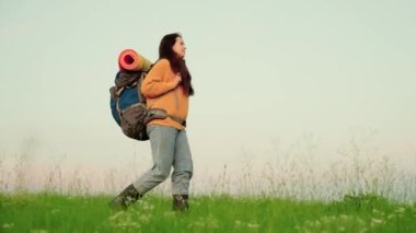 Kız gezgin, mavi gökyüzünün karşısındaki yeşil çimlerde seyahat eder meditasyon, eko-turizm, yürüyüş. Sırt çantalı, aktif, beyaz bir kadın yürüyüşe çıkıyor. Özgür kadın yazın çayırda yürüyen bir gezgindir.