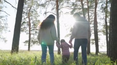 Mutlu aile ormanda yürüyor, bahar ve yaz aylarında el ele tutuşuyorlar. Baba, çocuk, kız, anne parkta oynuyorlar, mutlu çocuk ebeveynlerin elini tutuyor ve zıplıyor. Takım çalışması. Aile hafta sonu, çocukluk
