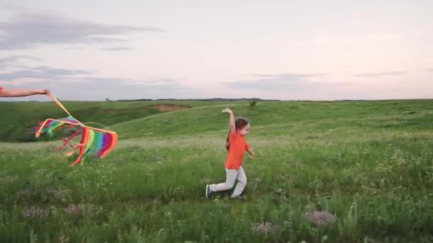 Дочь и мать запускают воздушного змея в небо, ребенок бежит по зеленой траве с воздушным змеем в руке. ребенок, девушка, играющая в парке со своей семьей. Детские мечты о полете, счастливые эмоции ребенка — стоковое видео