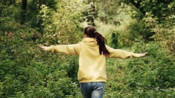 La joven corre alegremente en el parque. Concepto de persona feliz. Chica feliz corre a lo largo del camino del bosque agitando sus manos. Concepto de alegría, sueños, expresión de emociones. Chica corre a lo largo del camino entre árboles. — Vídeo de stock