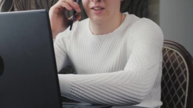 Modern dizüstü bilgisayar ve cep telefonuyla çalışan serbest çalışan biri. İş adamı, dizüstü bilgisayarla çalışıyor, akıllı telefonla konuşuyor. Ofiste, evde bilgisayar ve cep telefonu kullanan profesyonel bir erkek..