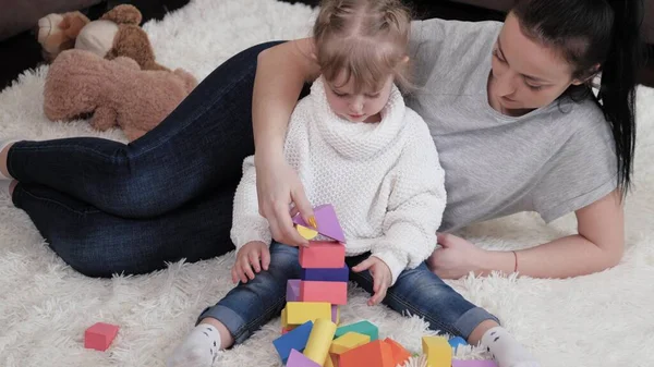 Mom, child plays with cubes in nursery on floor. Teaching child through play. Daughter and mother are playing building family home. Happy family. Educational games for children. Family weekend at home — Stock Photo, Image