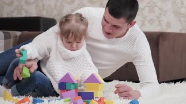 Baba, çocuk, kız yerde bebek odasında küplerle oynuyor. Çocuğa oyun yoluyla öğretmek. Çocuk ve baba aile evi inşa etme oyunu oynuyorlar. Çocuklar için eğitici oyunlar. Aile hafta sonu evde