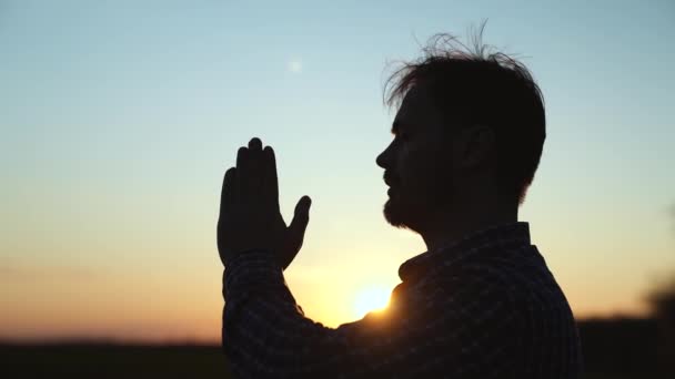 Христианин молится на закате крупным планом. Мужчины перед небом в лучах солнца молятся за семью и детей. Отдых и медитация в природе, здоровый образ жизни — стоковое видео