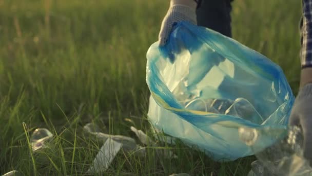 Волонтёр занимается уборкой пластикового мусора в парке на траве. Рабочие вручную поднимают пластиковую бутылку из травы. Экологически чистая планета без пластика. Загрязнение природы человеком — стоковое видео
