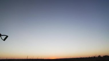 Siluet. Elinde kürek olan bir kadın çiftçi işten tarlaya gidiyor. Elinde kürek olan bir işçi gün batımında çiftlikte yürür. Tarım işi, tarım. Sebze yetiştiriyorum