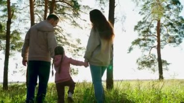 Aile hafta sonu, çocukluk. Mutlu aile ormanda yürüyor, bahar ve yaz aylarında el ele tutuşuyorlar. Baba, çocuk, kız, anne parkta oynuyorlar, mutlu çocuk ebeveynlerin elini tutuyor ve zıplıyor. Takım çalışması..