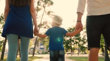 Aile tatili, hafta sonu. Parkta yürüyen mutlu ebeveynler ve çocuklar. Mutlu aile yazın gün batımında sessiz bir sokakta bir çocukla yürür. Baba, oğul, anne ve şehrin kaldırımında el ele tutuşun..