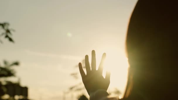 Ręka szczęśliwej dziewczyny sięga po słońce. Zachód słońca między dłońmi dziewczyny. Dziewczyna wyciąga rękę do słońca, promienie słońca świecą jej w palcach. Ręka dzieci marzy o słońcu. Szczęśliwa koncepcja rodziny — Wideo stockowe