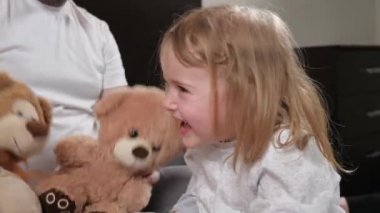 Babası kızıyla en sevdiği oyuncak ayısıyla oynuyor, bebek gülüşü eğleniyor. Mutlu çocuk babasıyla kanepede oyuncak ayıyla oynarken güler. Mutlu bir aile. Baba kız birlikte eğlenin.