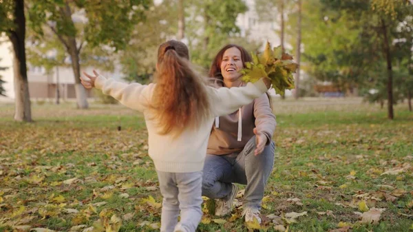 Barn, dotter springer till mamma kramar henne i höstparken, och ger bukett gula lönnlöv. Obekymmerslös barndom, glädjefylld barndom till mor. Lycklig familj. Liten unge leker med mamma glatt — Stockfoto
