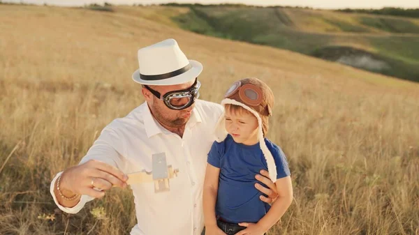 Gelukkige familie vader, kind, zoon spelen samen speelgoed houten vliegtuig in de zomer park. Een jongen met een helm, een vader met een bril buiten. Baby en papa spelen op de speelplaats, familiedroom en fantasieën — Stockfoto