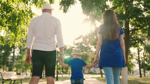 Gelukkige familie wandelingen met een kind op rustige straat in de zomer bij zonsondergang. Familie vakantie, weekend. Gelukkige ouders en kinderen wandelen in het park. Pap, zoon, moeder en hand in hand op de stoep in de stad in de zon. — Stockvideo