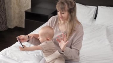 Mutlu bir aile, küçük çocuğu olan bir anne, evde modern bir akıllı telefon kullanıyor. Aile, teknoloji, annelik ve insan kavramı. Baba, küçük kız ve anneye video çağrısı. Modern ev eğitimi