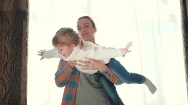 Anne çocuğuyla oynuyor, kızı kollarında daireler çiziyor, tatlı bebek mutlu ve evde gülüyor. Bebek ve anne evde oynuyorlar. Sevimli bir kız zevkle uçar ve annesiyle oynar..