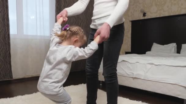 Father cheerfully plays an active game with his cute daughter, child at home in room. Family holiday, dad day off. Happy family, child, daughter and dad, holding hands, jumping, dancing in bedroom. — Stock Video