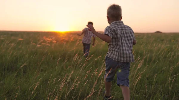 Mutlu çocuklar, çocuklar gün batımında çimlerin üzerinde birlikte parkta koşar. Parktaki insanlar neşeli koşu yapıyorlar. Mutlu aile, oğullar güneş ışınlarıyla tarlada koşuyor. Çocuğum, bebekler yazın dışarıda oynarken eğleniyor. — Stok fotoğraf
