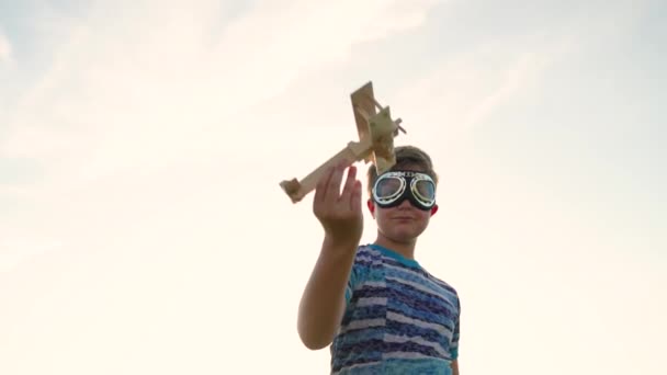 Niño despreocupado en gafas de piloto juega con el avión de juguete al aire libre. Niño feliz jugando con juguete avión de madera en frente del cielo. El chico tiene un avión de juguete en la mano. Familia feliz jugando en el parque — Vídeo de stock