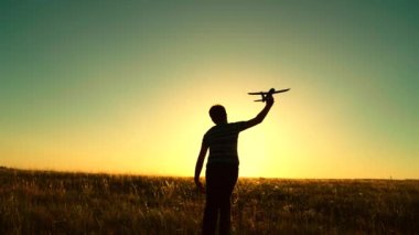 Mutlu çocuk silueti gün batımında oyuncak uçakla sahada koşuyor. Çocuk astronot olmayı hayal ediyor. Çocuk bir uçak pilotu olmayı hayal ediyor. Çocukların fantezisi, oyuncak uçakla koşan bir çocuk..