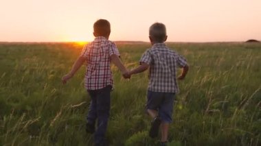 Erkek arkadaşlar gün batımına doğru koşar, küçük çocuklar güneş ışınlarında kovalamaca oynarlar, çocukluk hayalleri, parkta yeşil çayırlarda koşan komik çocuklar, el ele tutuşurlar, enerjik bir çocukluk.