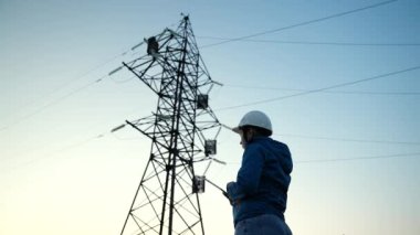 Koruyucu miğferde çalışan güç mühendisi kadın mühendis gün batımında yüksek voltajlı elektrik hatlarında çalışıyor. Dağıtım, elektrik kaynağı. Çevre dostu elektrik enerjisi. Elektrikçi