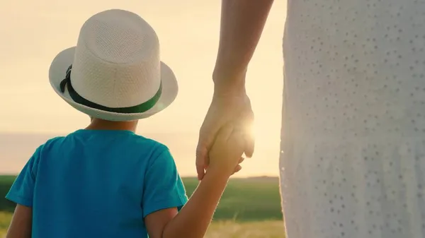 Happy family childhood. Mom and son are walking together holding hands in sun. Happy family outing. Child in summer hat. People in park. Kid, boy, mom outdoor. Family holiday, Parents, children, dream Stock Image