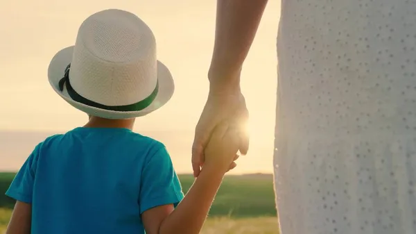 Infância familiar feliz. A mãe e o filho andam juntos de mãos dadas ao sol. Feliz passeio em família. Criança de chapéu de verão. Pessoas no parque. Miúdo, rapaz, mãe ao ar livre. Férias em família, Pais, crianças, sonho Imagens De Bancos De Imagens