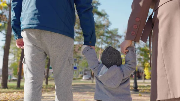 Ευτυχισμένοι γονείς και παιδιά που περπατούν στο πάρκο το φθινόπωρο. Ο μπαμπάς, ο γιος, η μαμά και να κρατήσει τα χέρια στο πεζοδρόμιο της πόλης στον ήλιο. Οικογενειακές διακοπές, Σαββατοκύριακο. Ευτυχισμένη οικογένεια περπατά με ένα παιδί σε ήσυχο δρόμο — Φωτογραφία Αρχείου