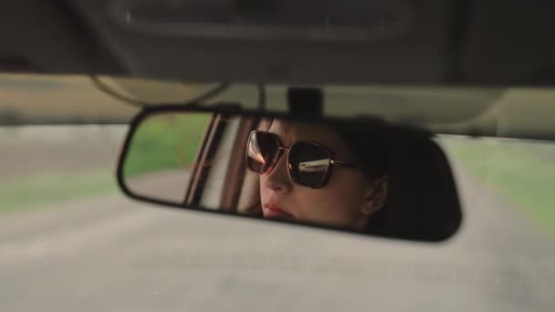 Uma jovem mulher livre viajando de carro. Jovem motorista em óculos de sol no espelho retrovisto.A menina motorista está dirigindo seu carro. Fim de semana, carro, aventura, estrada e esportes. Taxi. — Vídeo de Stock