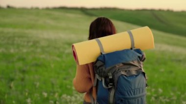 Özgür kadın gezgin yazın çayırlarda yürüyor. Kız gezgin, güneşin altında yeşil tepe boyunca seyahat eder meditasyon, eko-turizm, yürüyüş. Aktif, beyaz, sırt çantalı bir kadın yürüyüşe çıkıyor.