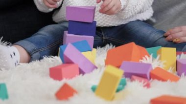Kız ve anne bir aile evi inşa etme oyunu oynuyorlar. Anne, çocuk yerde bebek odasında küplerle oynuyor. Mutlu bir aile. Çocuklar için eğitici oyunlar. Aile hafta sonu evde. Bir çocuğa oyun yoluyla öğretmek.