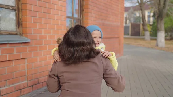 Dítě, syn běží k mámě a na podzim ji objímá v parku na ulici. Šťastná rodina. Bezstarostné dětství, radostný běh dítěte k jeho matce. Malé dítě se baví na ulici s rodiči. Matka objímá svého syna — Stock fotografie