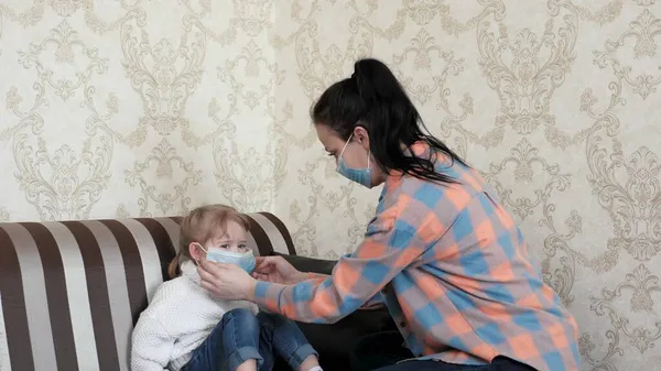 Mom teaches how to put on medical mask for her little daughter. Stay home mom. Coronavirus or COVID-19. Mother shows her child how to put on medical mask. Family at home, prevention of viral diseases — Stock Photo, Image