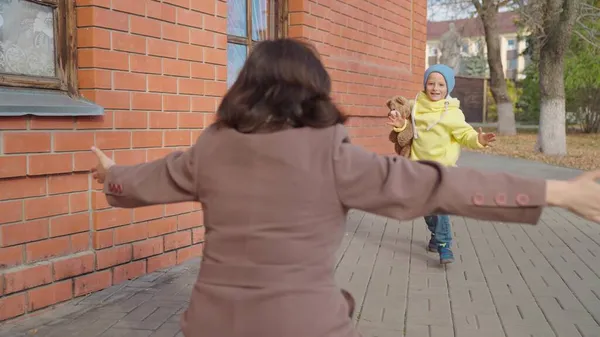 Дитя, сын бежит к маме обнимает ее в парке на улице осенью. Счастливая семья. Беззаботное детство, радостное бегство ребенка к матери. Маленький ребенок веселится на улице с родителями. Мать обнимает сына Стоковая Картинка
