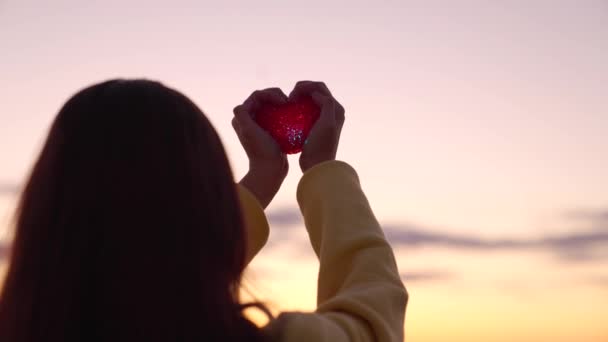 Jeune fille tient beau coeur rouge dans ses mains sur fond de coucher de soleil. Femme amoureuse d'une lampe de poche rouge symbole du cœur. Saint Valentin. Santé, prenez soin de votre cœur, médecine cardiaque. — Video