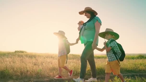 Mutlu aile, anne, çocuklar yaz parkına sırt çantasıyla gider. Takım çalışması. Anne ve küçük oğulları kırsal bölgelerde seyahat ediyorlar. Aile tatili. Çocuklar ve anne toprak bir yolda el ele yürüyorlar.. — Stok video